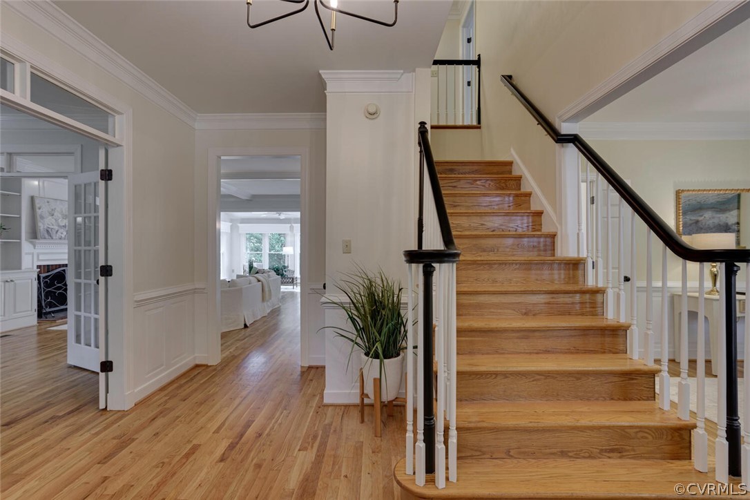 Foyer with a broad hardwood staircase, dark railings, white wainscoting, and hardwood floors.