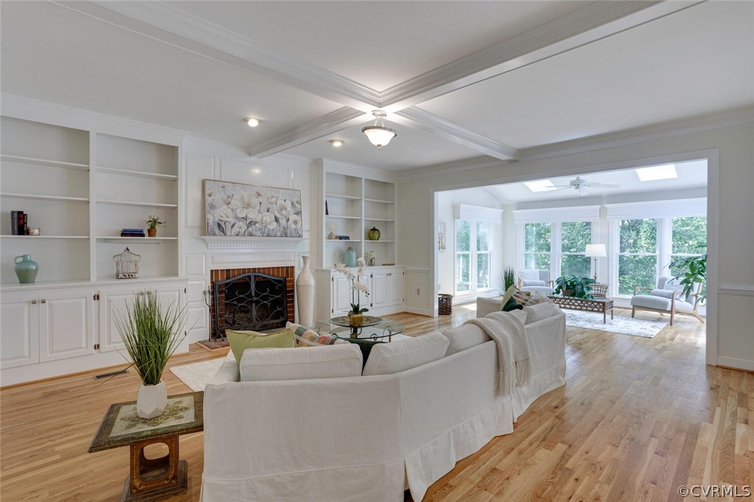 Living room with built-in shelves, brick fireplace, coffered ceiling, and an adjoining bright sunroom.