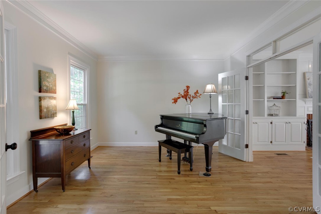 Music room with a black grand piano, hardwood floors, and open French doors beside built-in shelves.