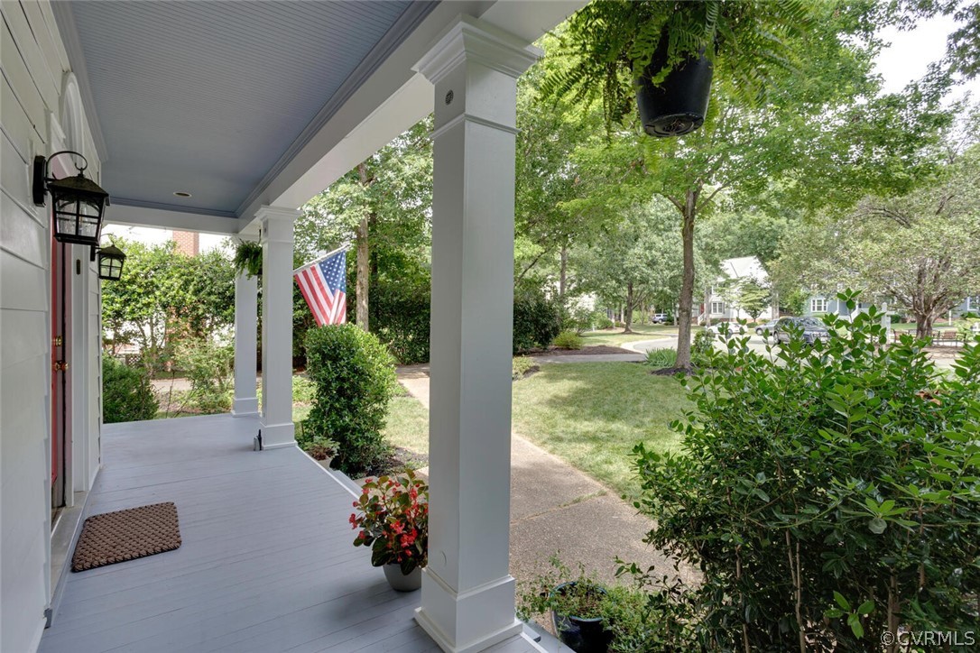 Covered front porch with white columns, an American flag, and a tree-lined front yard.