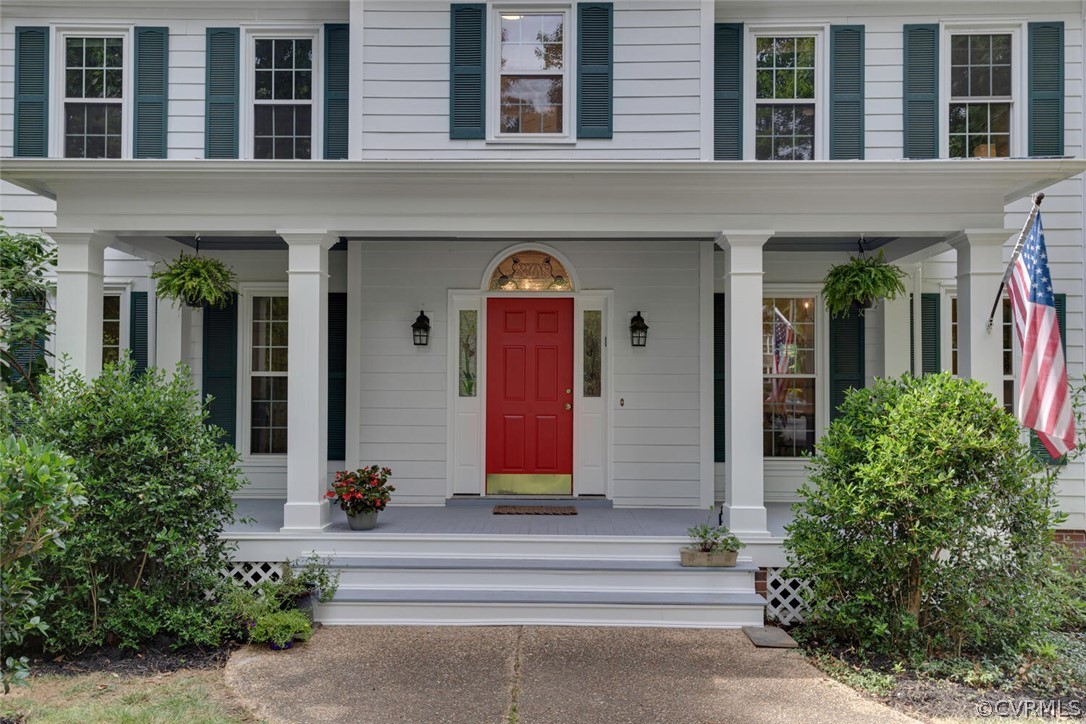 White two-story home with green shutters, a columned porch, and a red front door.