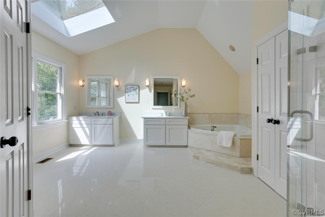 Bright bathroom with a skylight, dual vanities, corner soaking tub, and glass-enclosed shower.