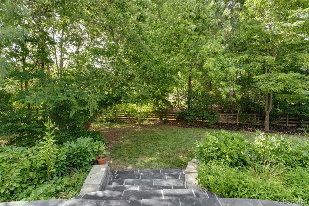 Landscaped backyard with stone steps, a small lawn, mature trees, and a wooden fence.