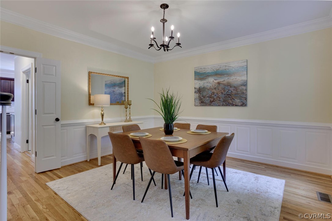 Dining room with a wooden table, brown chairs, white wainscoting, and hardwood floors.