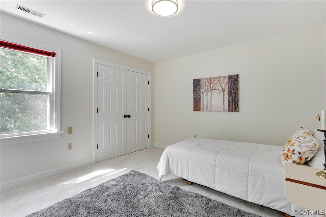 Bright bedroom with a white bed, gray rug, and window overlooking trees.