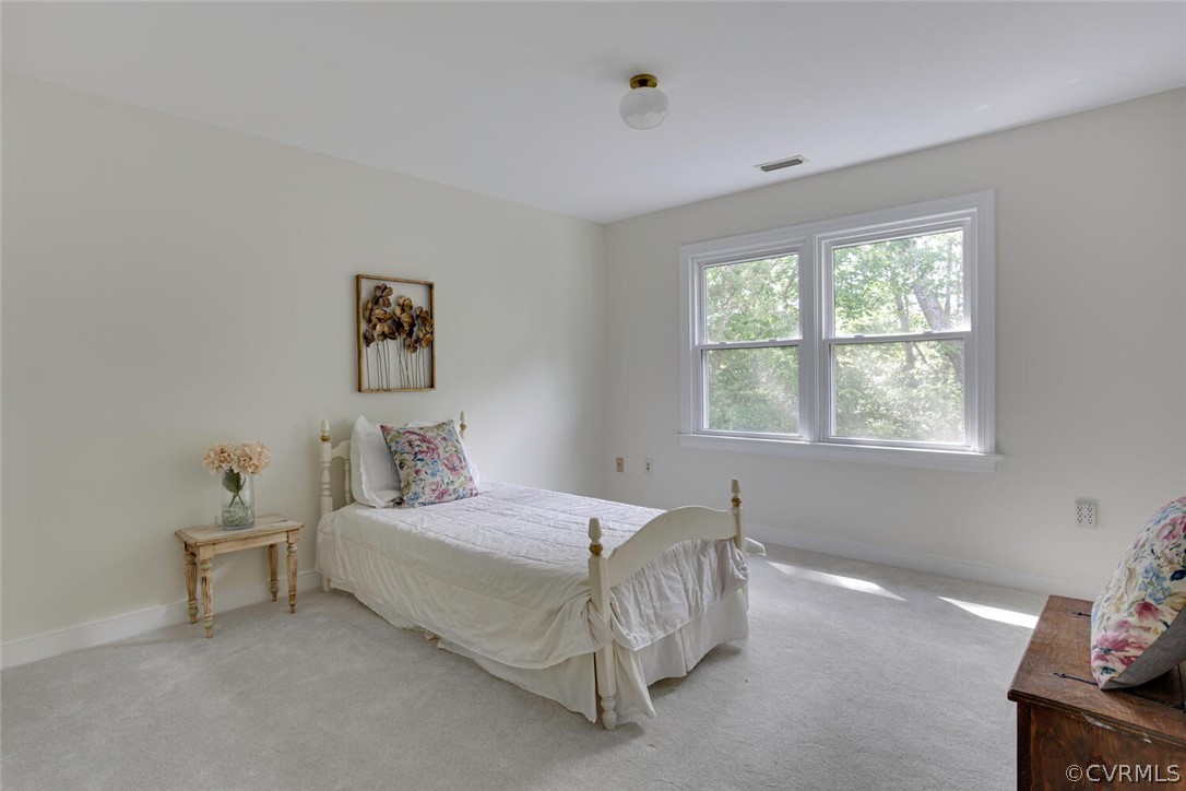 Bedroom with a white bed, floral pillows, and two windows overlooking leafy trees.