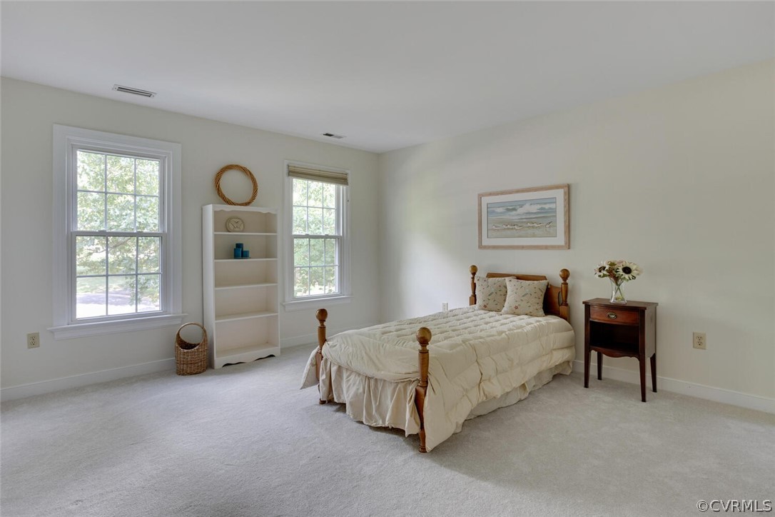 Bedroom with a wooden bed, cream quilt, and two windows overlooking leafy trees.