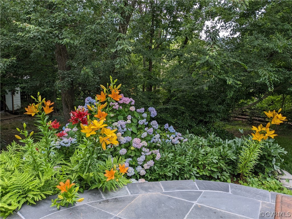 Landscaped garden with orange lilies and hydrangeas beside a curved stone patio.