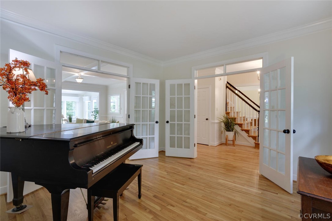 Grand piano in a bright hardwood-floored room with open French doors to the staircase hall.