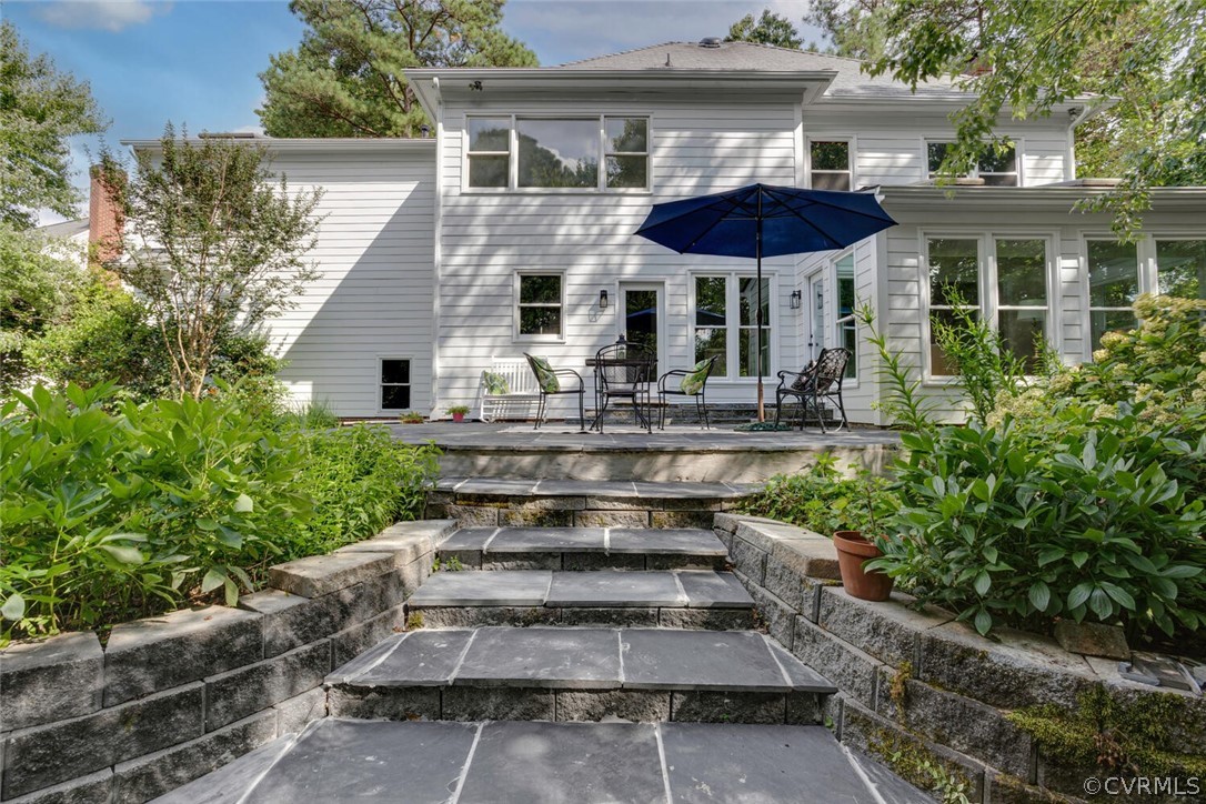 White two-story home with a patio and navy umbrella above broad stone garden steps.