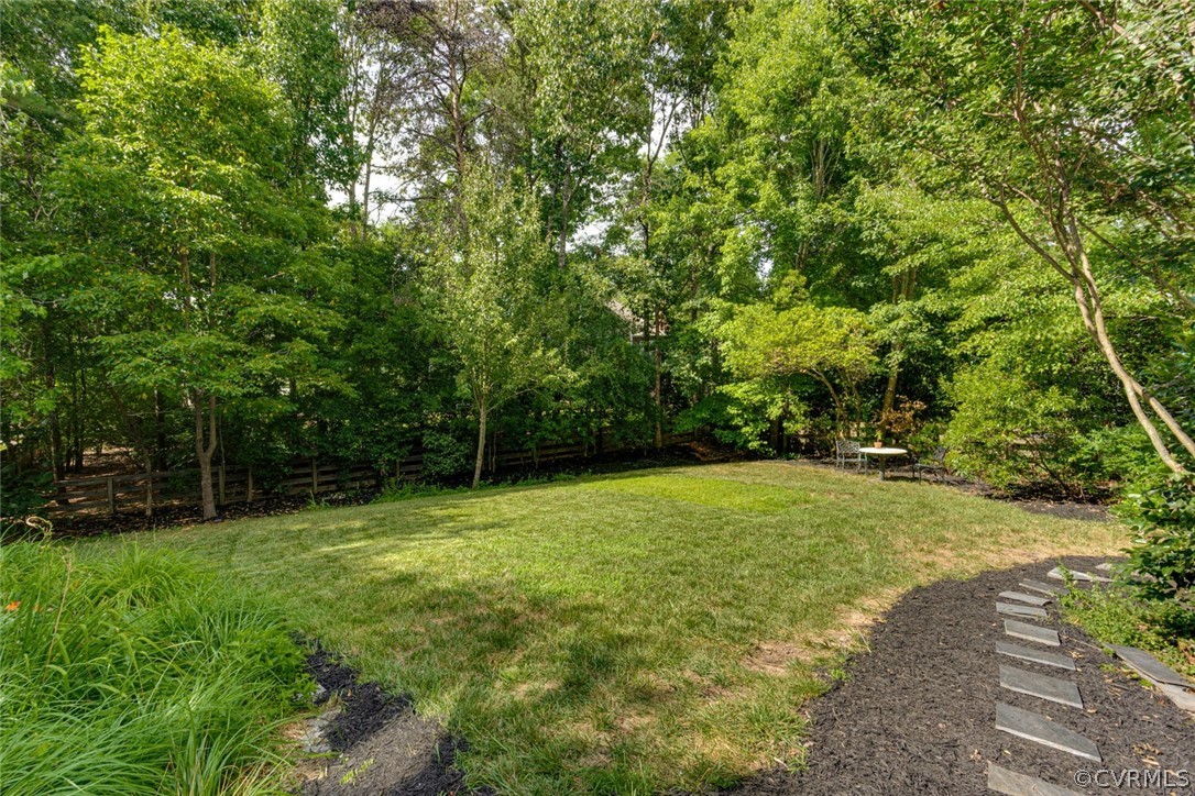 Backyard lawn bordered by mature trees, with a patio table and stepping stones.