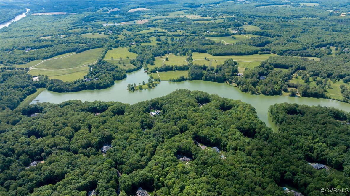 Aerial view of wooded homes beside a winding lake and open fields.