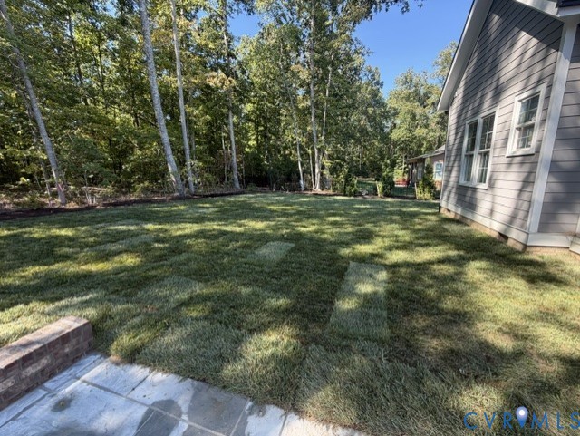 Backyard lawn with mature trees, a stone patio, and the gray-sided house.