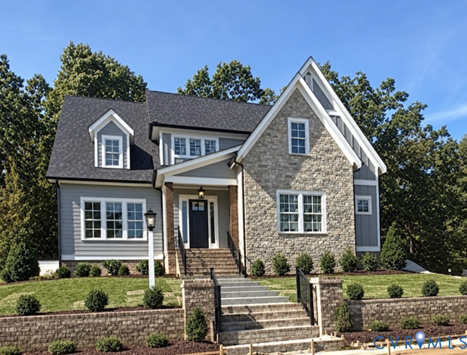 Two-story home with gray siding, stone facade, and a landscaped front entrance.