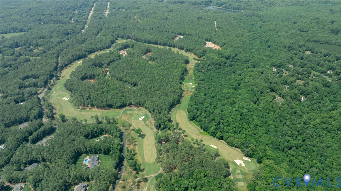 Aerial view of a golf course winding through dense woods, with a home and pool nearby.