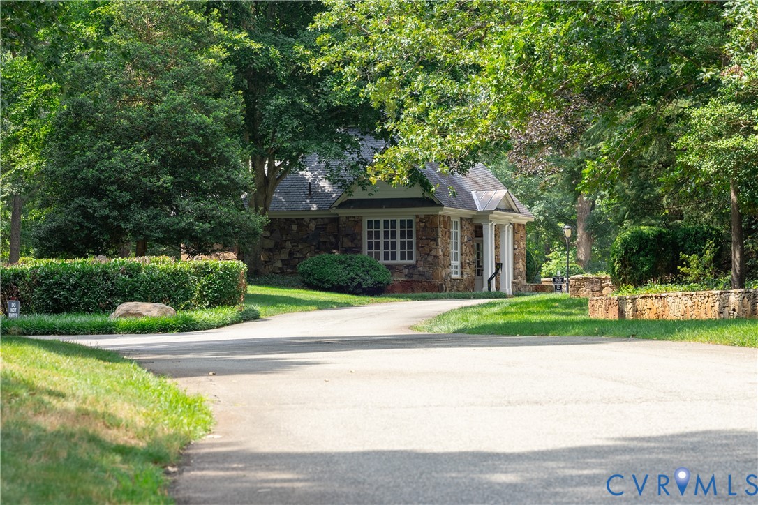 Stone building beside a curving road, framed by mature trees and a low stone wall.