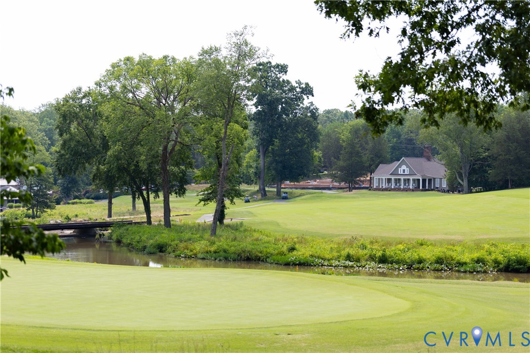 Golf course with a creek and bridge in the foreground and a house beyond the fairway.