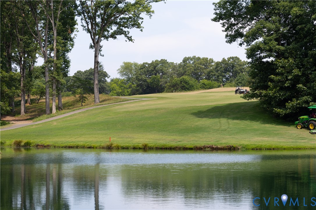 Golf course fairway and cart path beyond a pond, framed by mature trees.