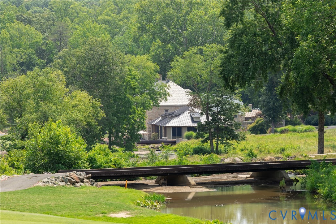 Home nestled among trees beyond a grassy lawn, with a bridge crossing a pond in front.