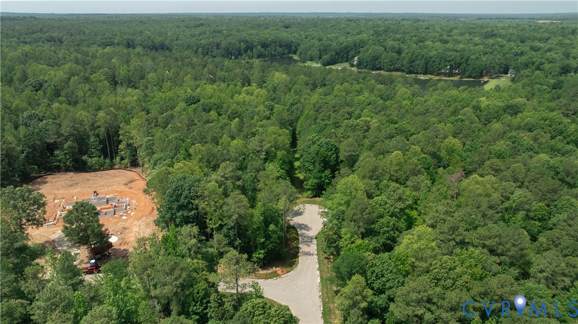 Aerial view of wooded property with a cleared construction site beside a curving road.
