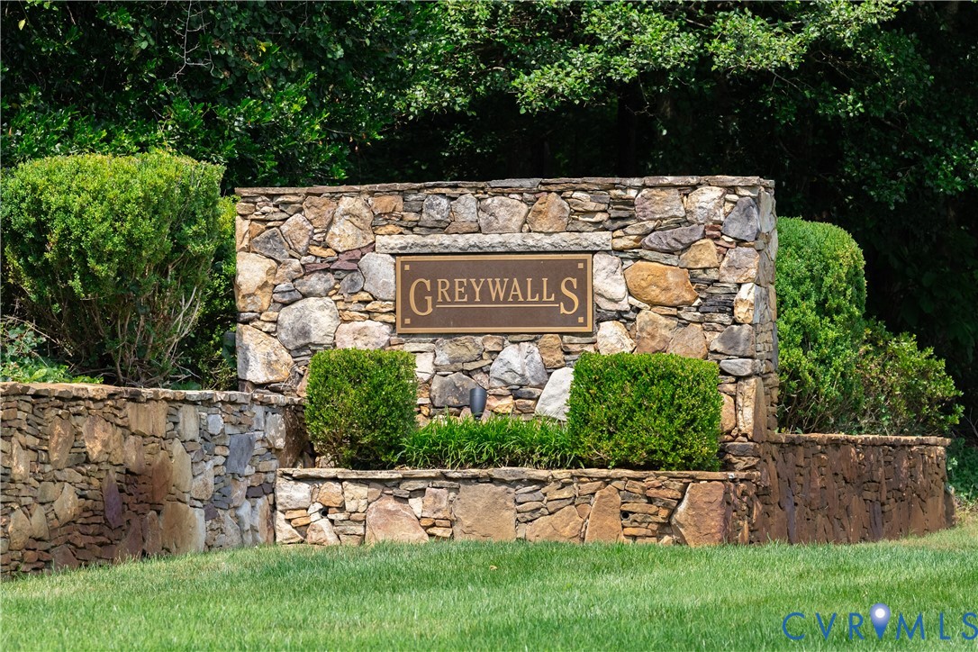 Stone Greywalls entrance sign surrounded by shrubs and trees beside a lawn.