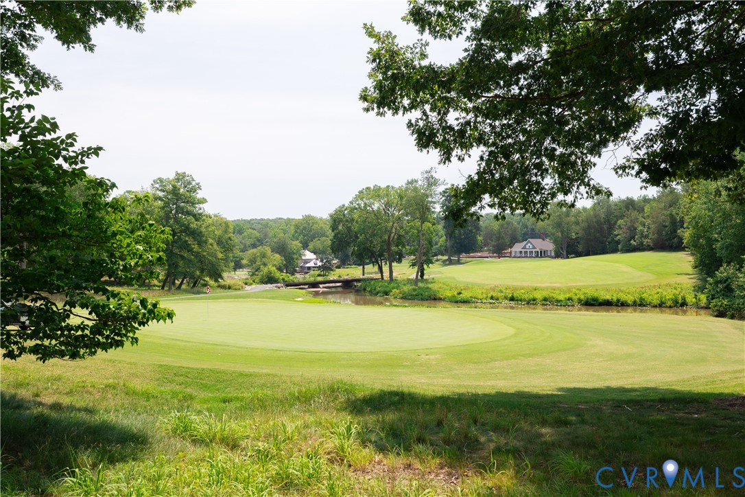 Golf course with a putting green, pond, and homes beyond mature trees.