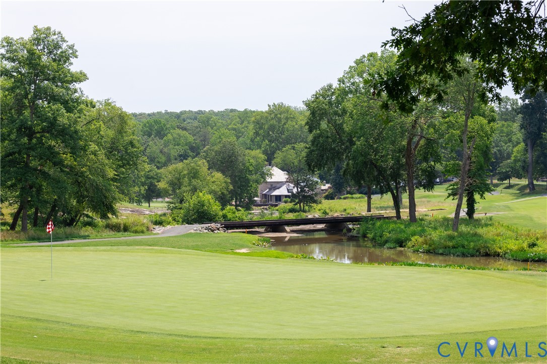 Golf course with a putting green, pond, and bridge framed by mature trees.