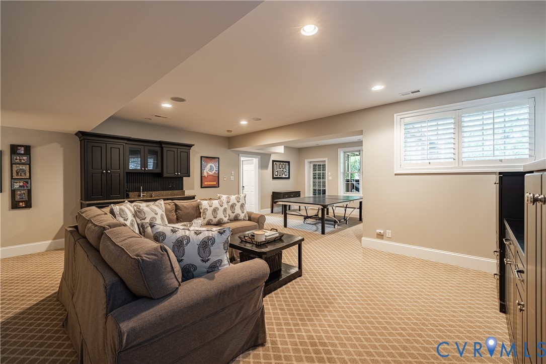 Basement recreation room with a sectional sofa, dark built-in cabinets, patterned carpet, and a ping-pong table.