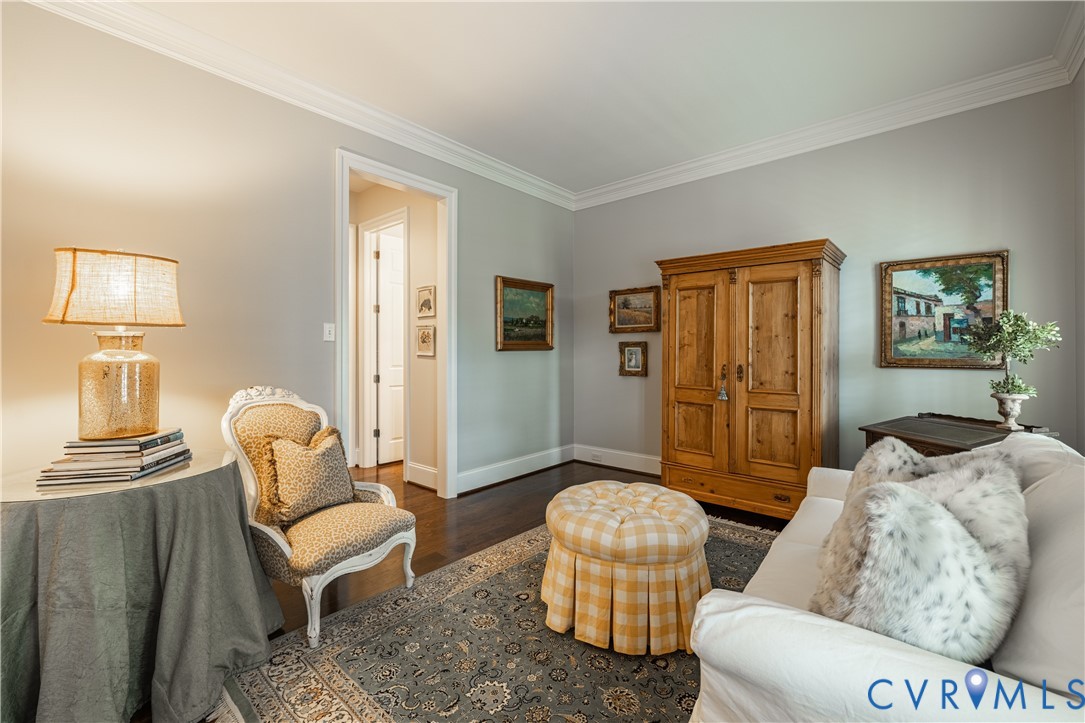 Living room with a wooden armoire, white sofa, patterned rug, and round plaid ottoman.