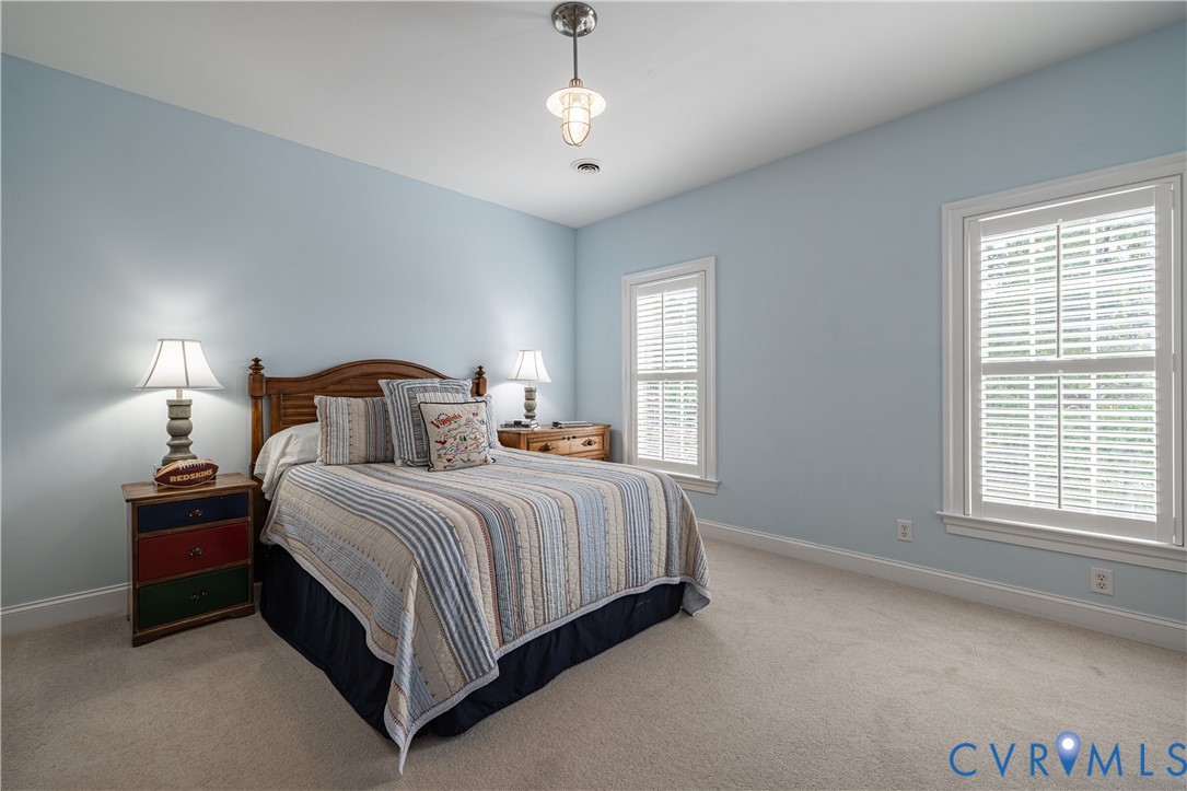 Bedroom with a wooden bed, striped quilt, pale blue walls, and two windows with white blinds.