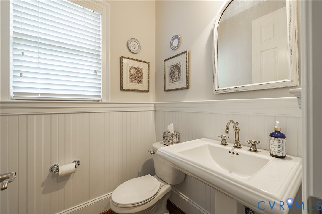 Bathroom with a white sink, brass faucets, paneled walls, and a large framed mirror.