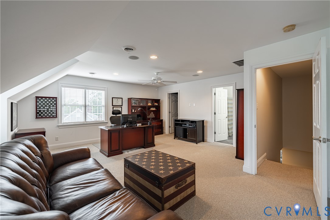 Furnished home office with a leather sofa, dark wood desk, and sloped ceiling.