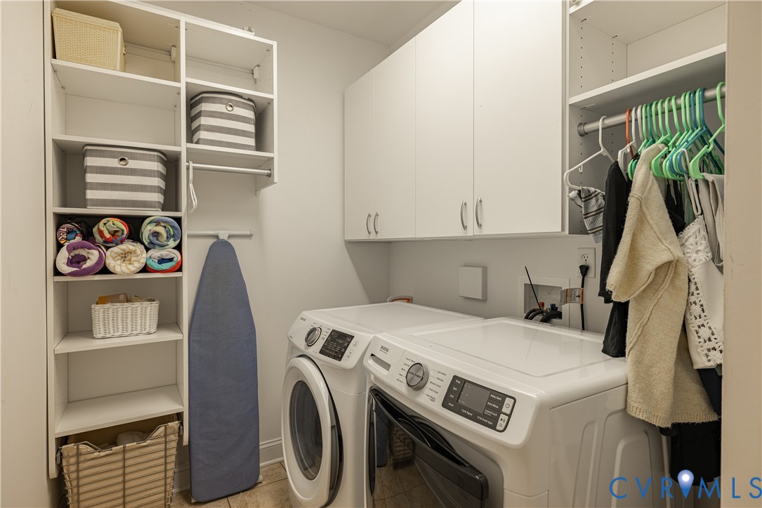 Laundry room with washer and dryer, white cabinets, storage shelves, and hanging clothes.