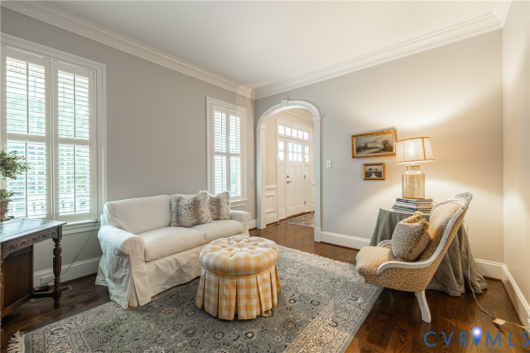 Living room with shuttered windows, a white sofa, patterned armchair, and arched entryway.
