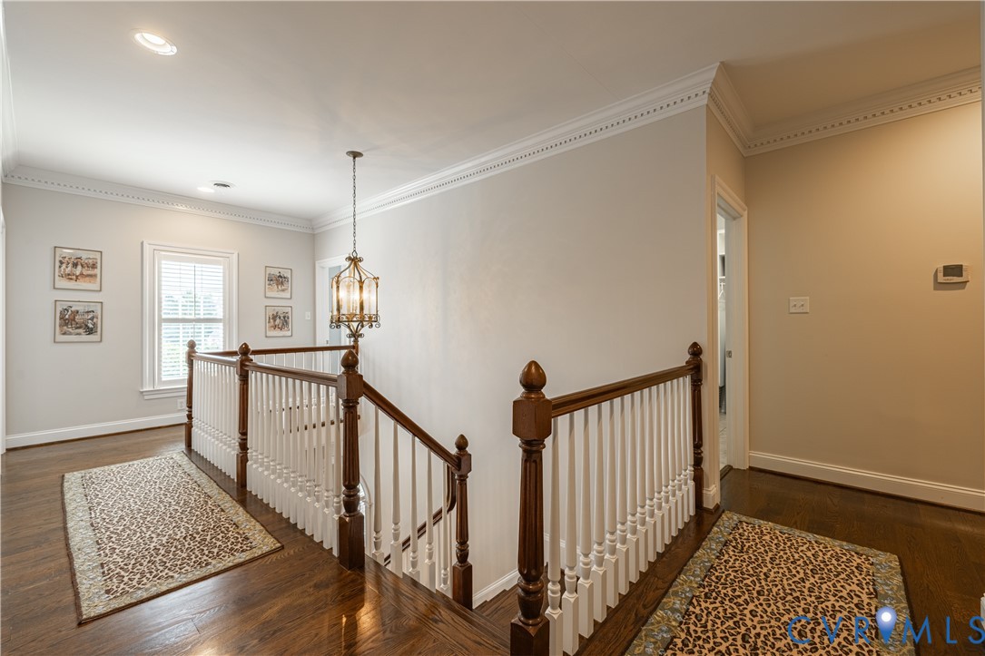 Upstairs landing with a dark wood staircase, white balusters, patterned runners, and a hanging chandelier.