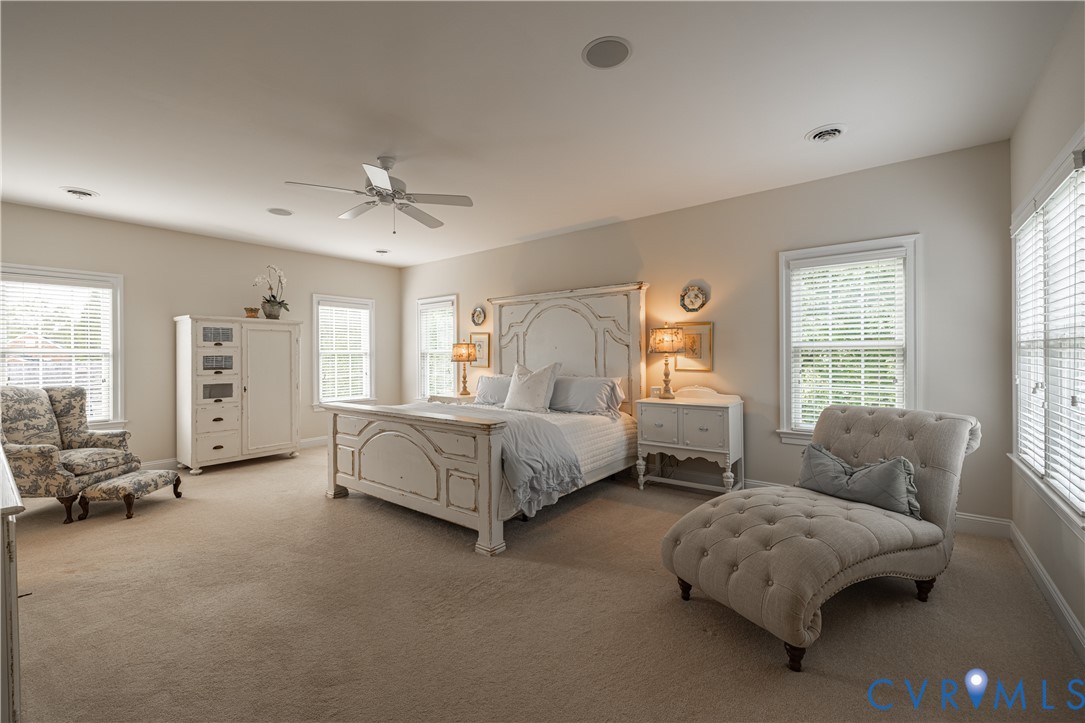 Staged bedroom with a carved white bed, tufted chaise lounge, and windows on three walls.