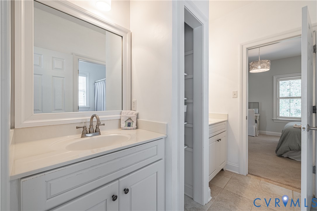 Bathroom vanity with a large mirror, opening to a carpeted bedroom.