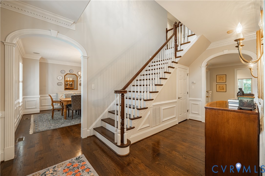 Foyer with a dark hardwood staircase, white wainscoting, and arched openings to adjoining rooms.