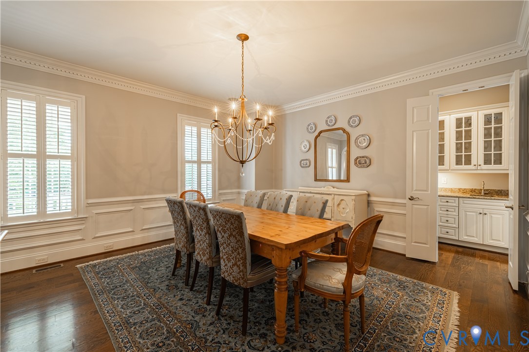 Dining room with a wooden table, upholstered chairs, patterned rug, and chandelier.