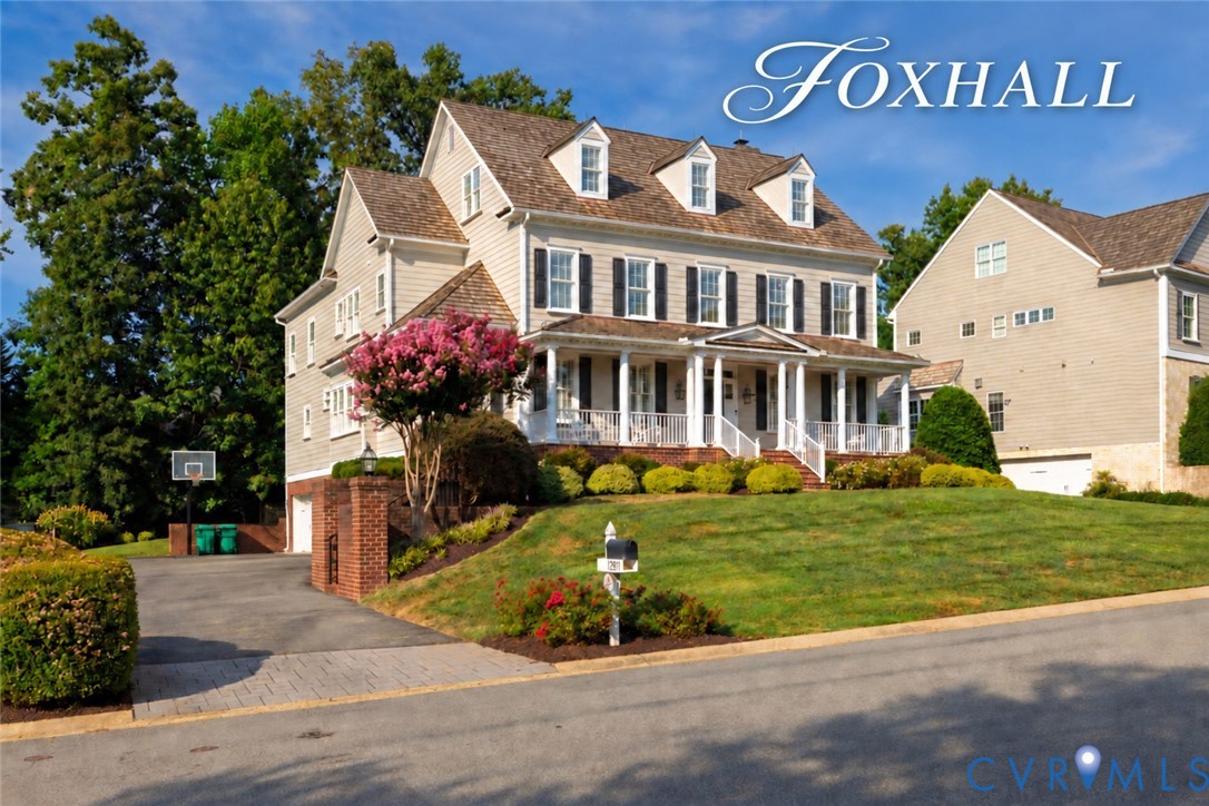 Beige Colonial home with a white wraparound porch, dormer windows, and a landscaped lawn.