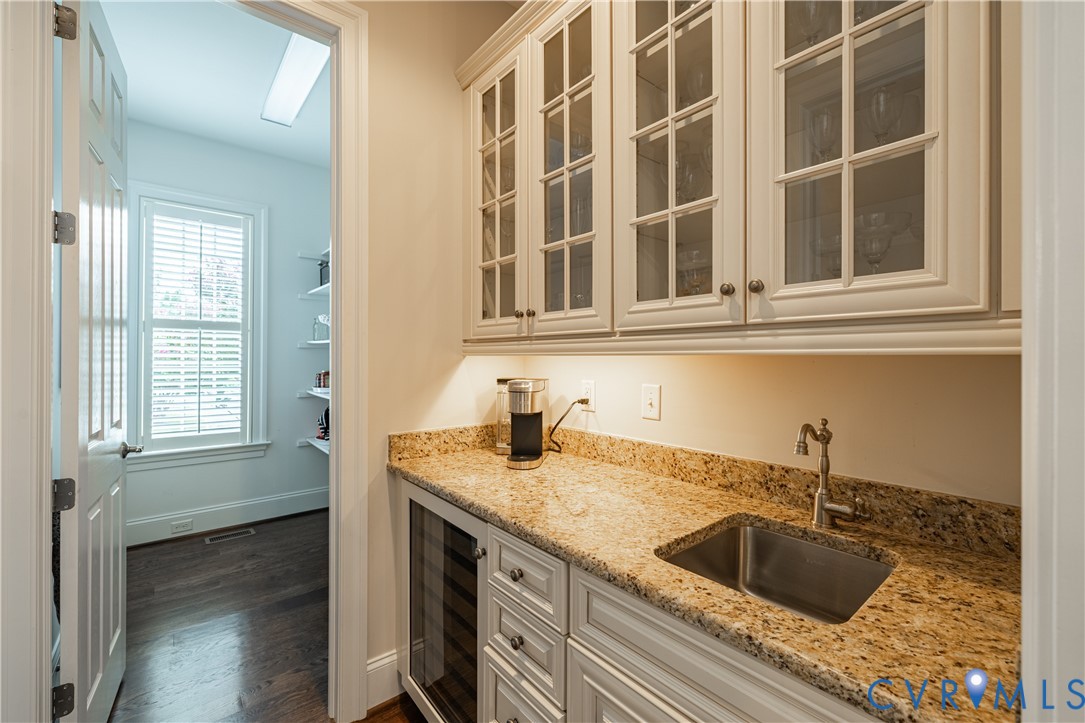 Beverage station with glass-front cabinets, granite counter, sink, and under-counter wine refrigerator.