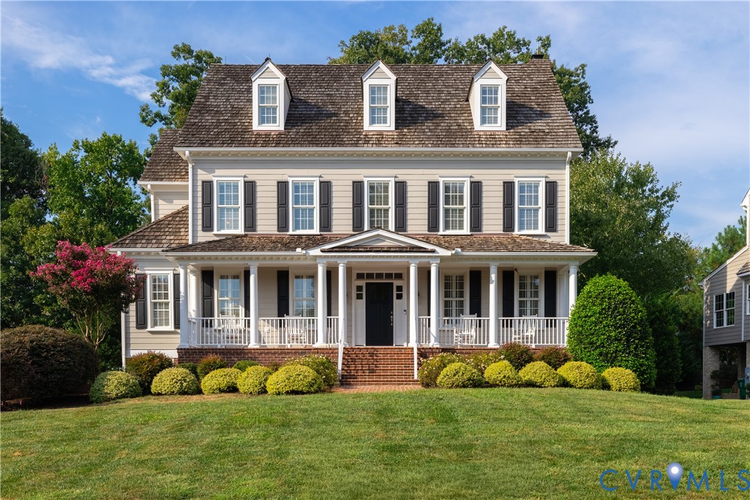Two-story beige house with three roof dormers, black shutters, and a columned front porch.