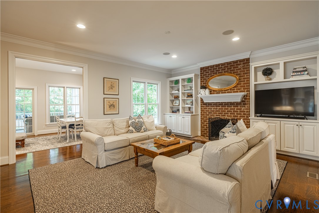 Living room with cream sofas, a brick fireplace, built-in cabinetry, and hardwood floors.
