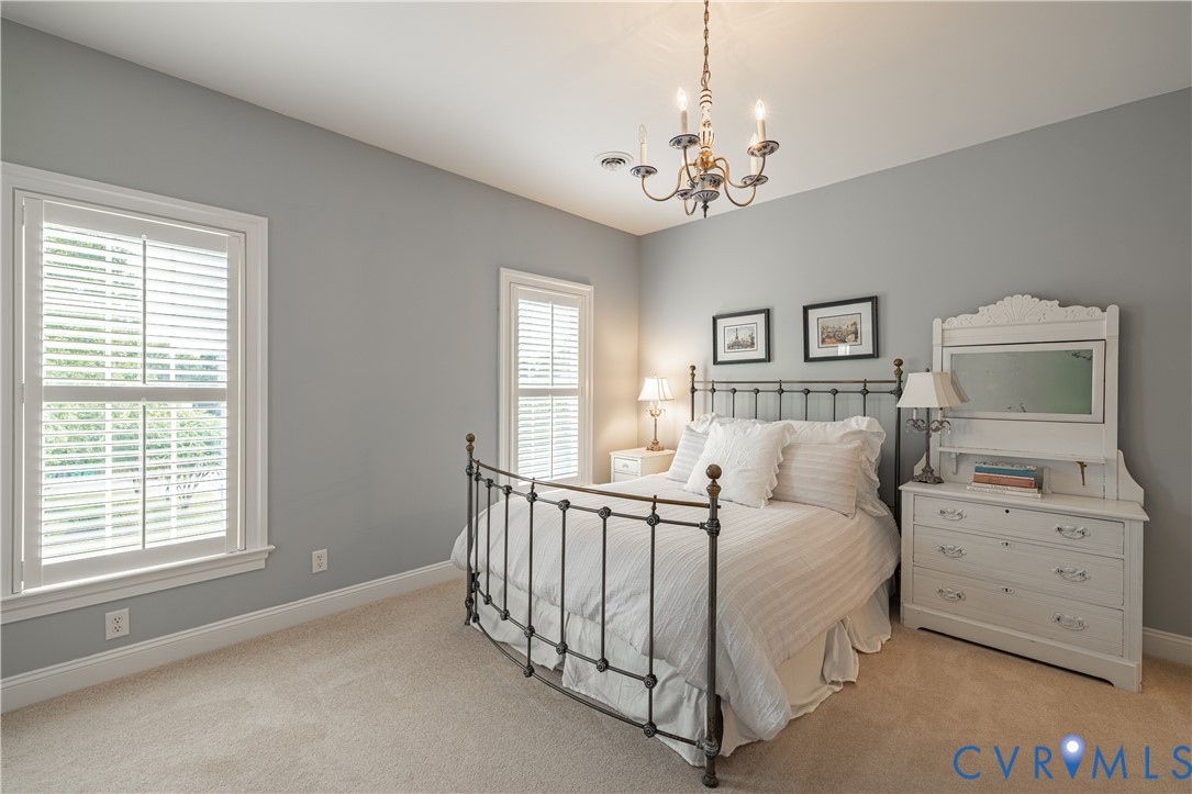 Furnished bedroom with a black metal bed, white bedding, gray walls, and shuttered windows.