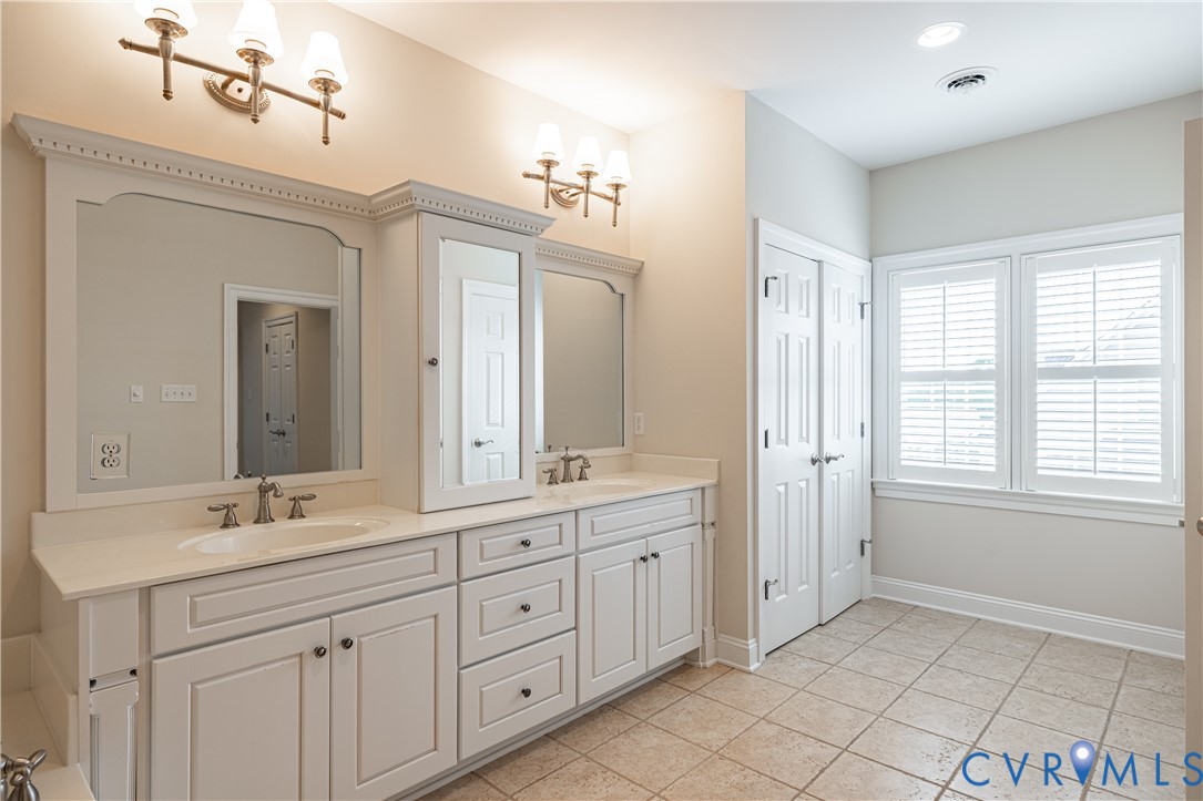 Bathroom with a long white double vanity, framed mirrors, tiled floor, and a window with blinds.