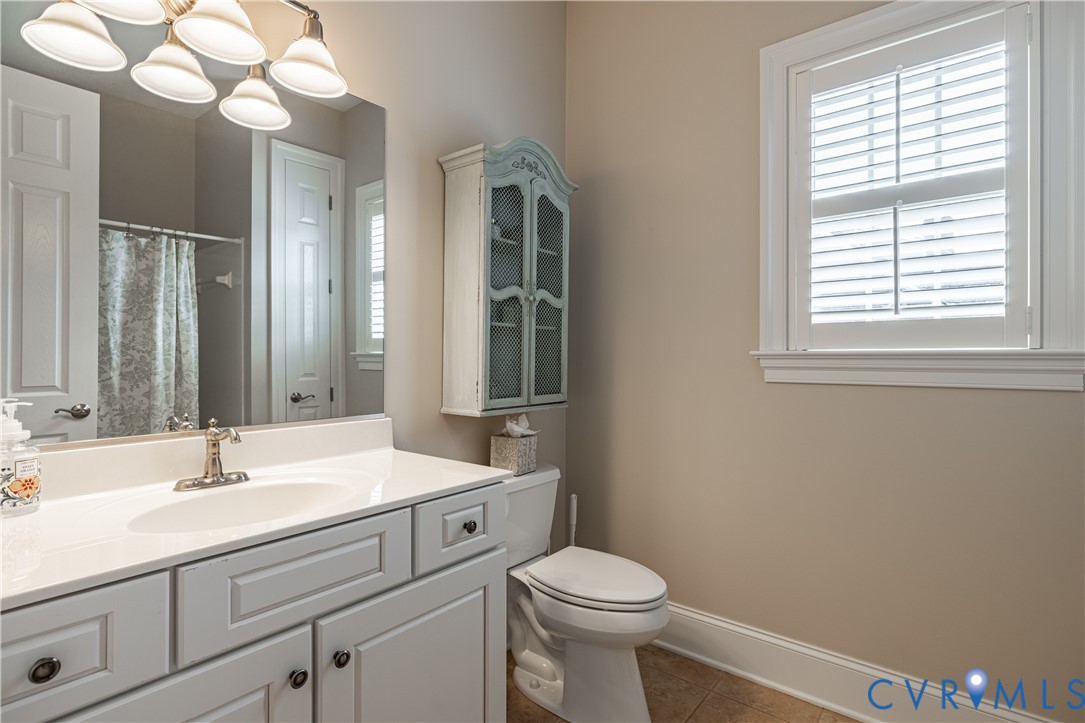 Bathroom with a white vanity, glass-front wall cabinet, and window with plantation shutters.