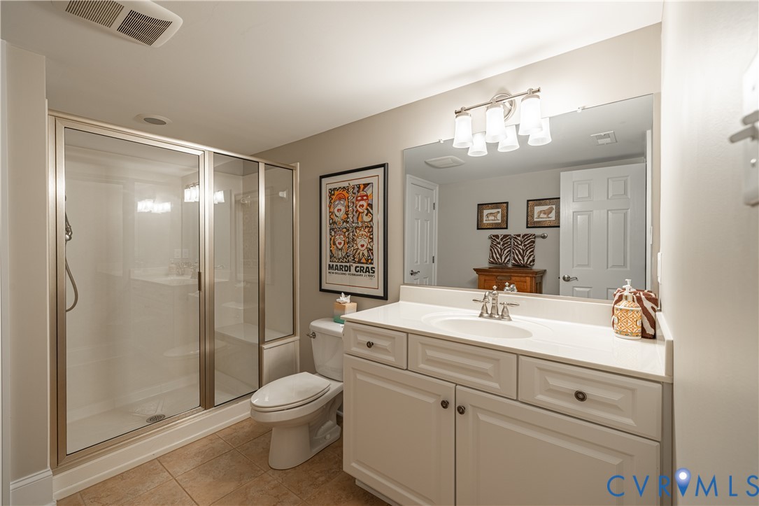 Bathroom with a glass-enclosed shower, white vanity, oval sink, and framed Mardi Gras poster.