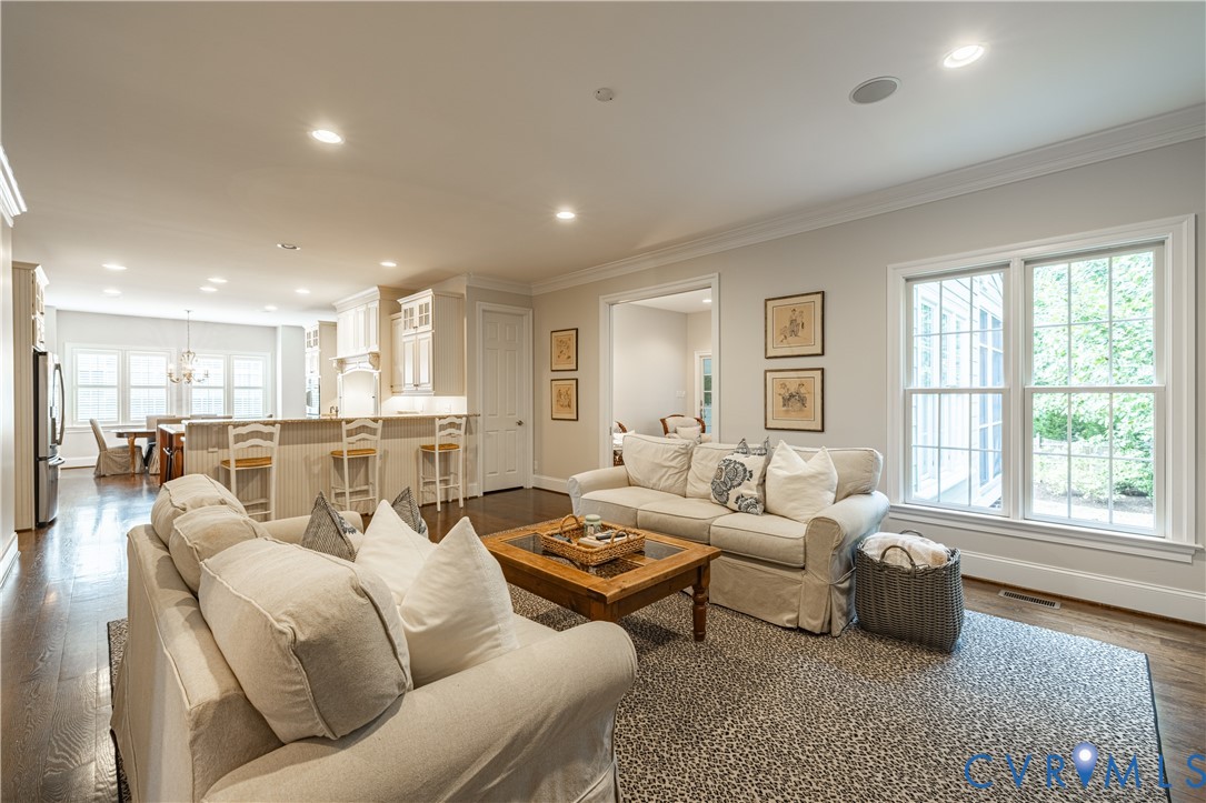 Staged living room with cream sofas, a wooden coffee table, and large windows beside the open kitchen.