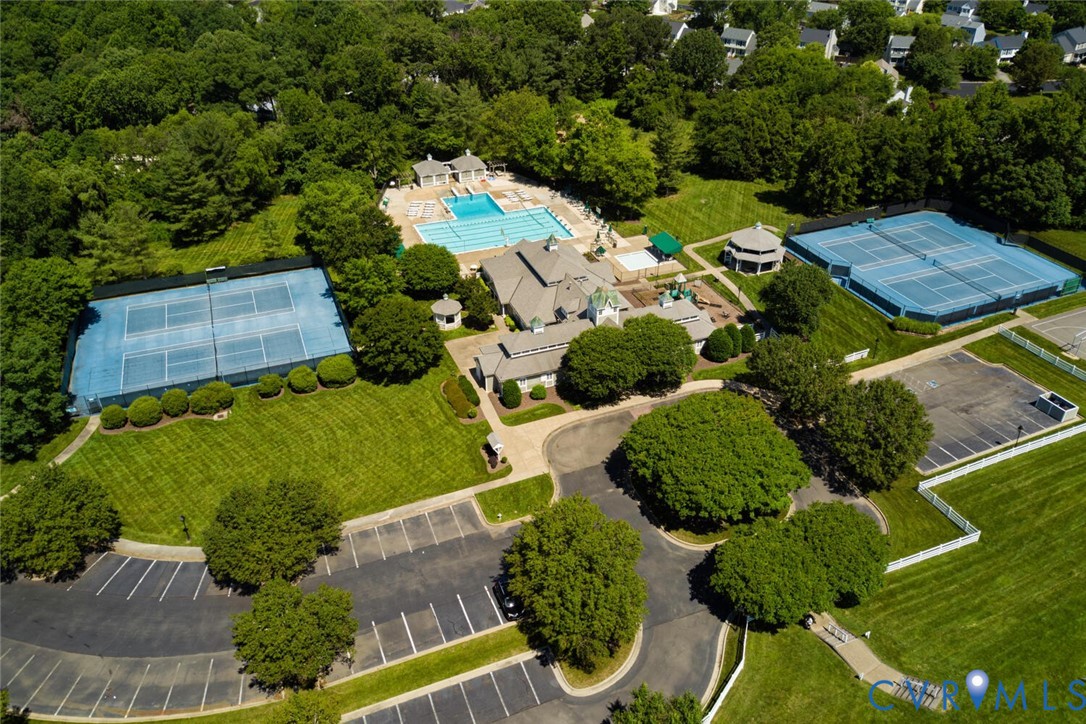 Aerial view of a community clubhouse, swimming pool, and tennis courts surrounded by trees.