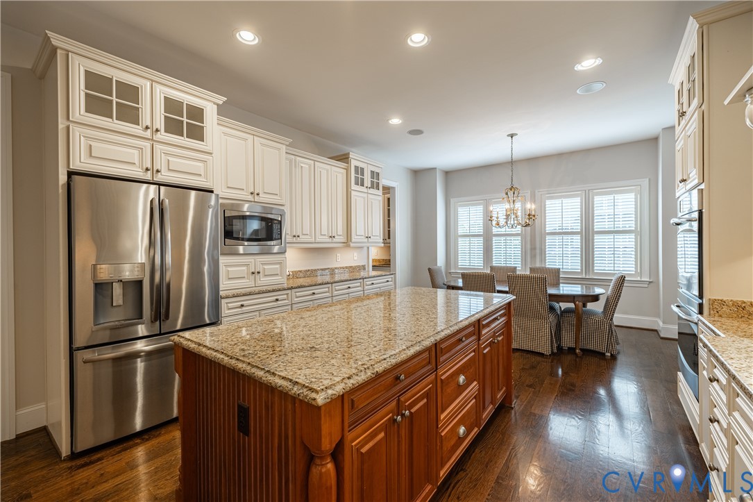 Kitchen with a large granite-topped wood island, stainless appliances, and a dining area by shuttered windows.